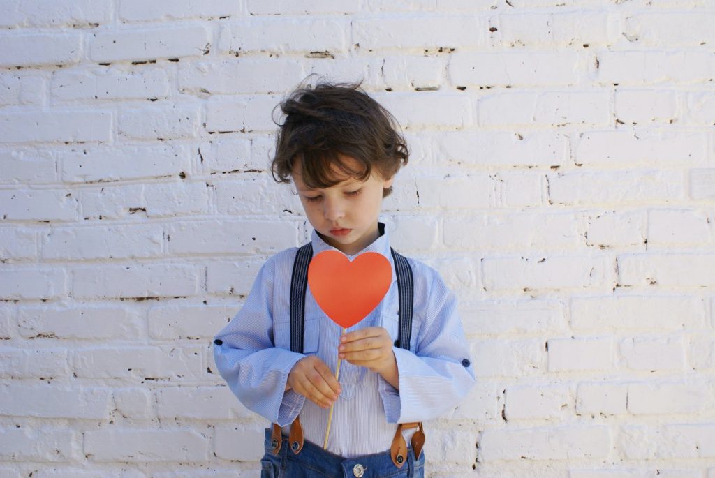 small child holding a heart, he is sad due to loss of parent